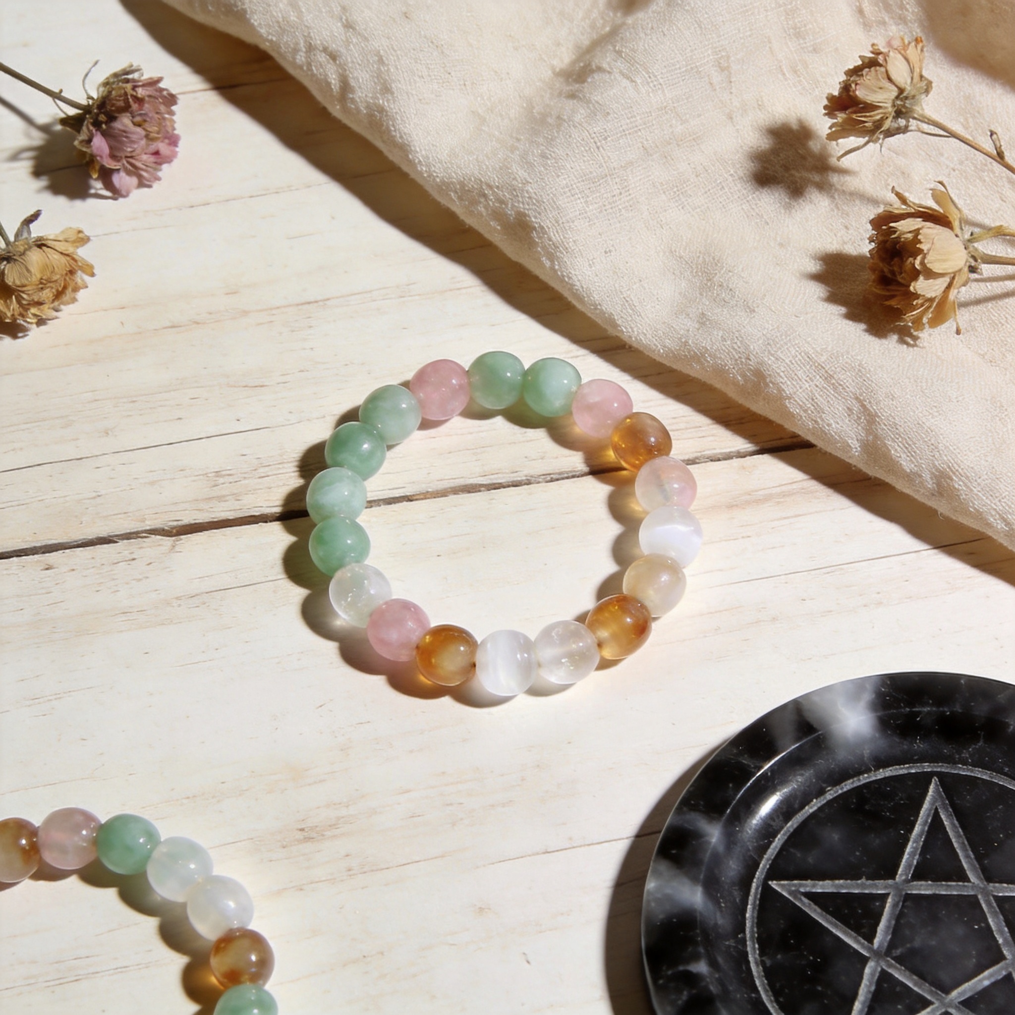 Multicolor natural stone bracelet resting on a light wooden table with linen, dried flowers and a black selenite plate